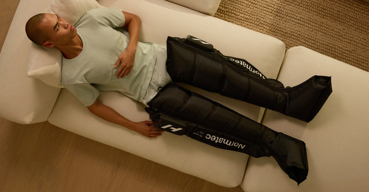 Man lying on a couch with Normatec compression sleeves on his legs